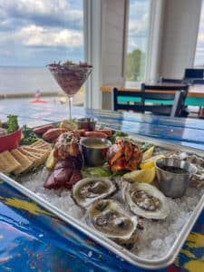 A picture of the sea-cuterie board at Shaggy's on the Rez. This dish features stuffed lobster tails, pickled marinated crab claws, murder point oysters, fish dip and crackers, served on a metal tray.