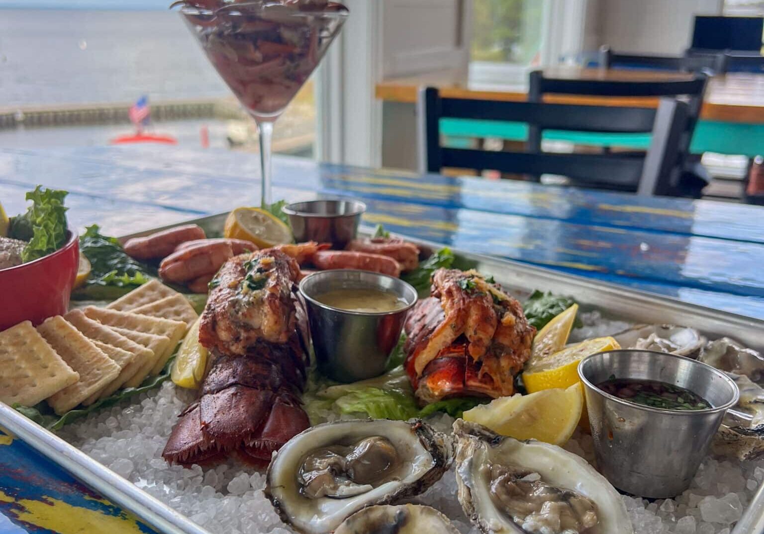 A picture of the sea-cuterie board at Shaggy's on the Rez. This dish features stuffed lobster tails, pickled marinated crab claws, murder point oysters, fish dip and crackers, served on a metal tray.